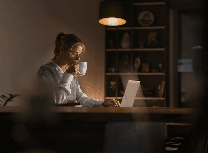 Uma mulher sentada à mesa com um laptop e uma xícara de café