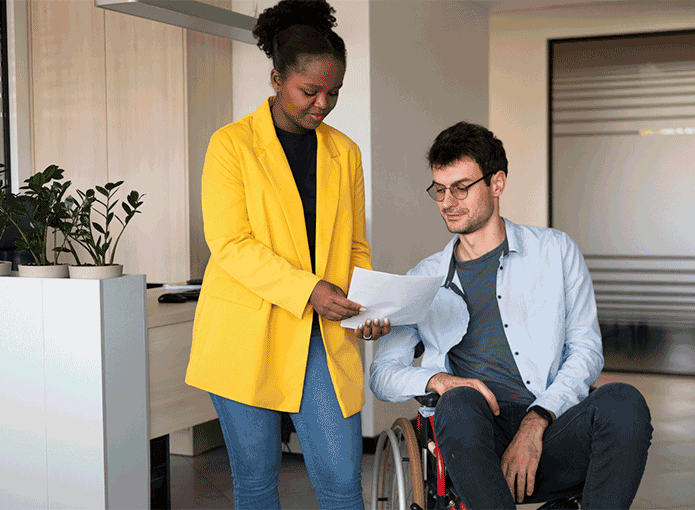 Um homem em uma cadeira de rodas e uma mulher com uma jaqueta amarela