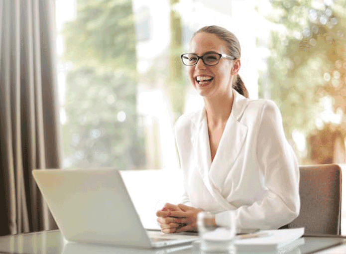 Uma mulher sentada e sorrindo em frente a um notebook