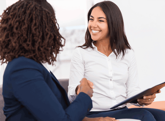 Duas mulheres sentadas e se cumprimentando numa entrevista de emprego