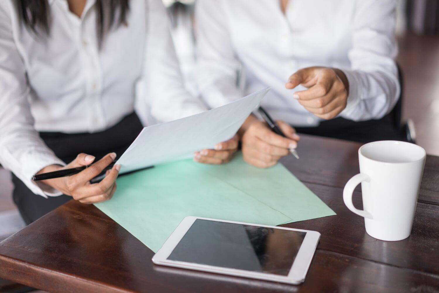 Duas profissionais analisando documentos e discutindo estratégias com tablet sobre a mesa.