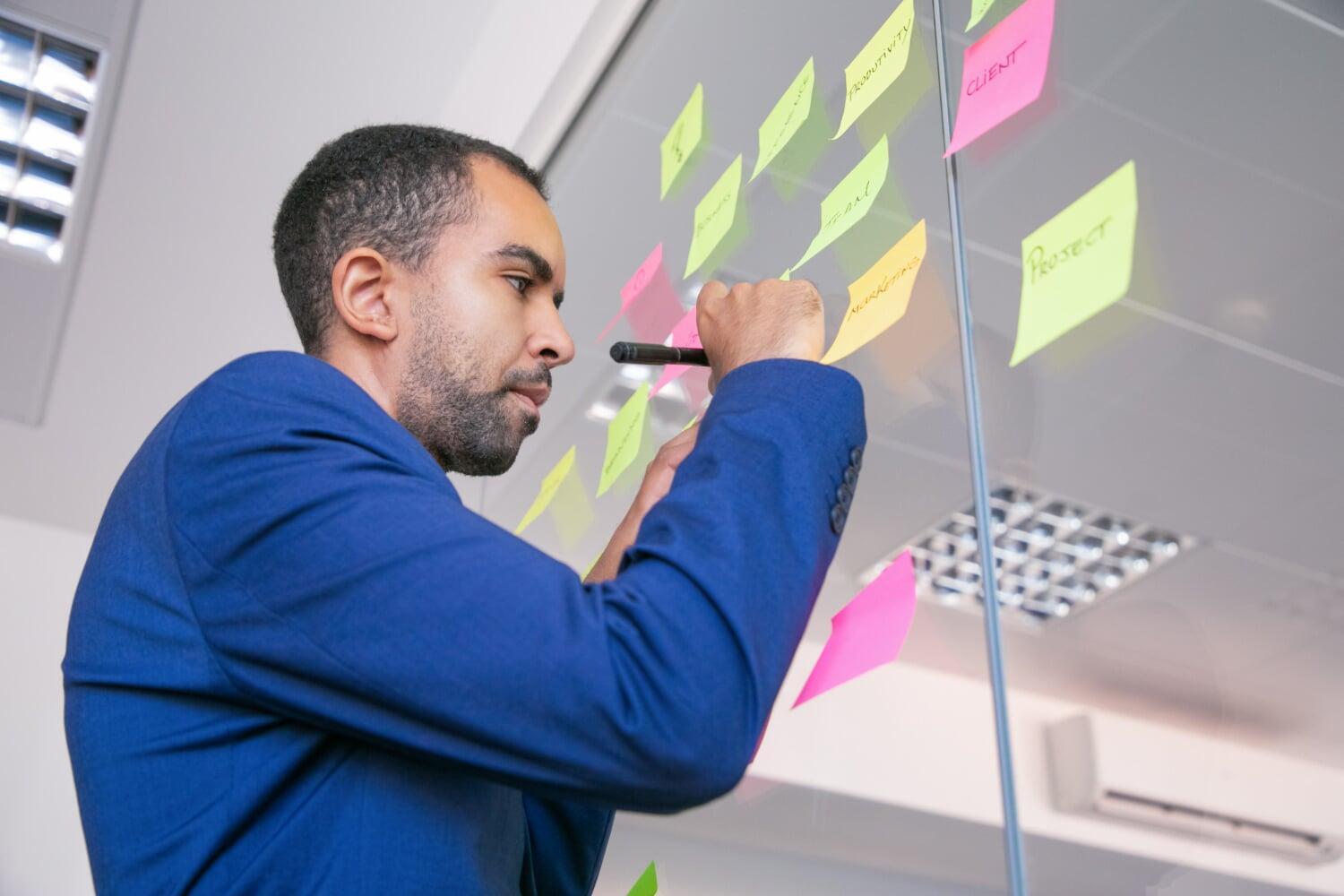 Homem escrevendo em post-its durante planejamento em ambiente corporativo